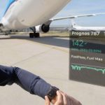 Guy standing next to plane looking at Smartwatch to check reporting.