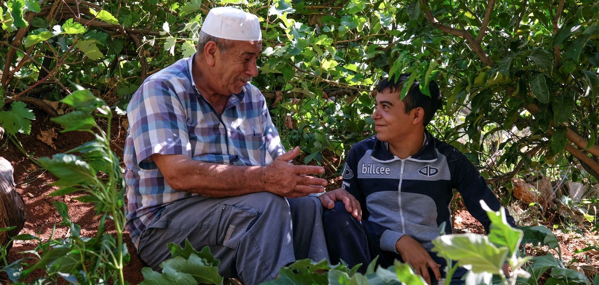 An older man and a younger boy smiling, surrounded by trees