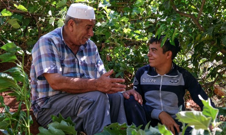 An older man and a younger boy smiling, surrounded by trees