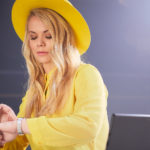 Woman with yellow hat and coat looking at her watch