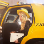 Woman with yellow hat stepping out of yellow cab with a Surface