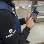 Politieagent die een smartphone in de hand heeft.