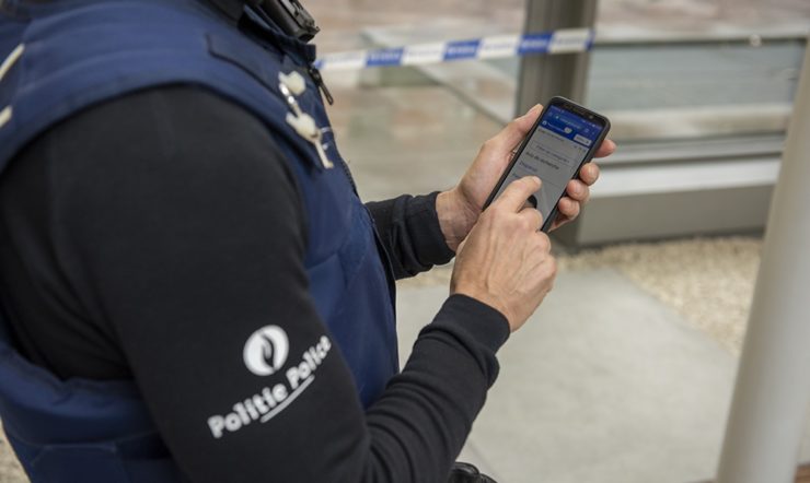 Politieagent die een smartphone in de hand heeft.