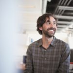 A smiling man wearing a gray shirt while looking up.