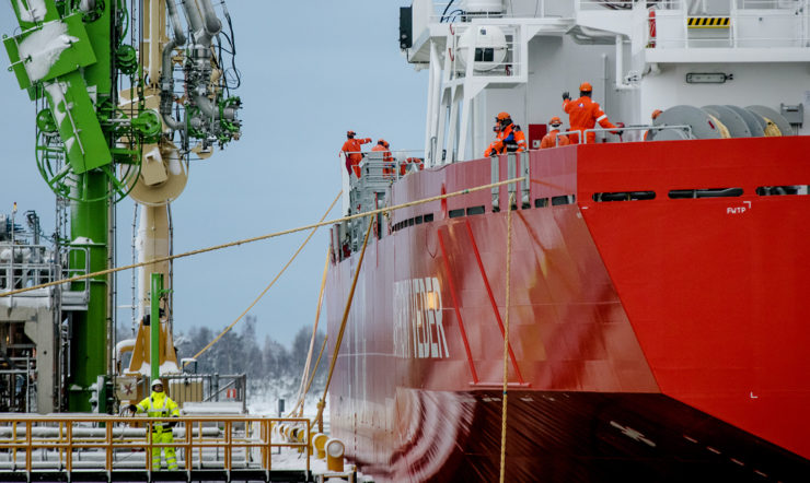 A large red ship with a few men onboard stationed at the shipyard