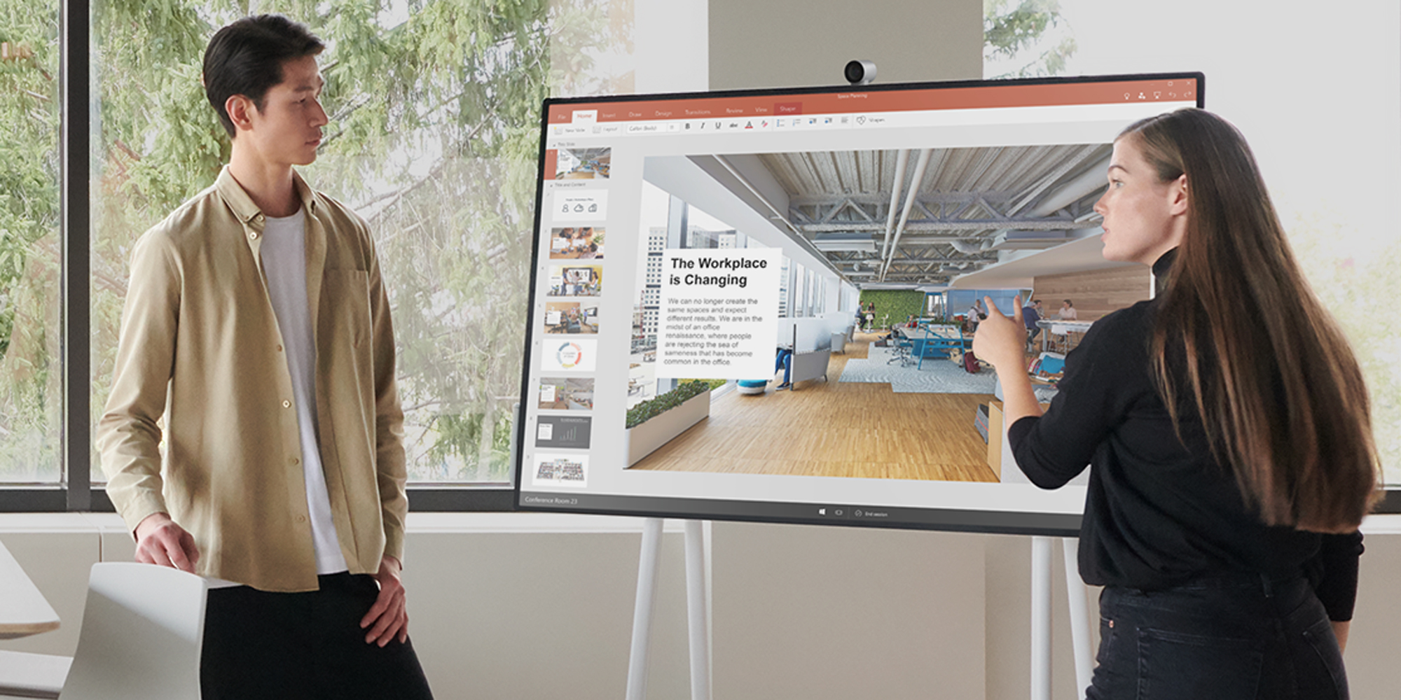 um homem e uma mulher em pé à frente de um Surface Hub 2S