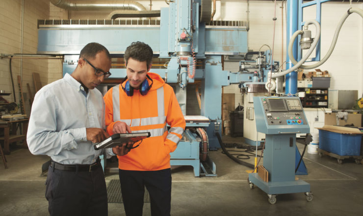 Een man in een fabriek die naar een tablet kijkt