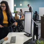 Two people sitting and standing in front of a computer