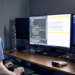mies seisoo vieressä tietokoneen näytön pöydällä