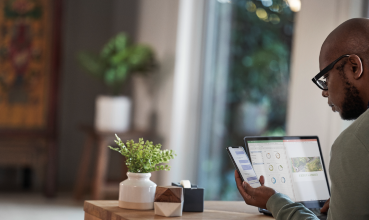 Male working remotely from his home office on a Dell Latitude 13 device, running Microsoft Excel and PowerPoint, checking phone.
