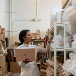 Contextual image of woman holding Surface Laptop 3 in Sandstone working in a warehouse.