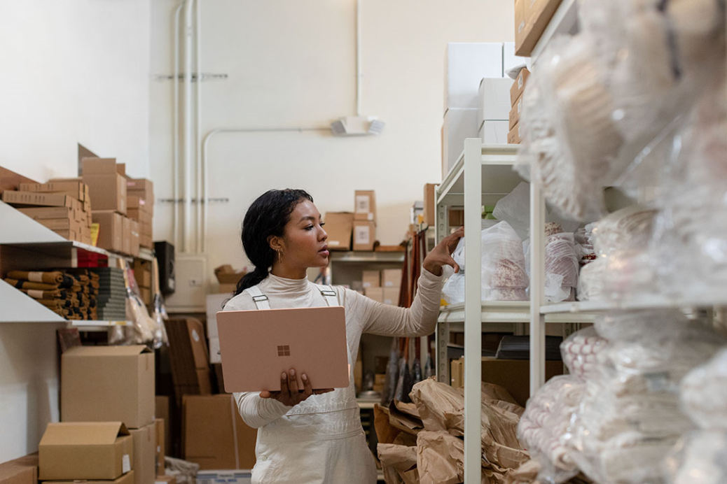 Contextual image of woman holding Surface Laptop 3 in Sandstone working in a warehouse.