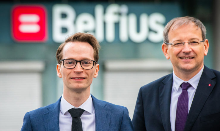 Two people wearing a suit and tie smiling at the camera