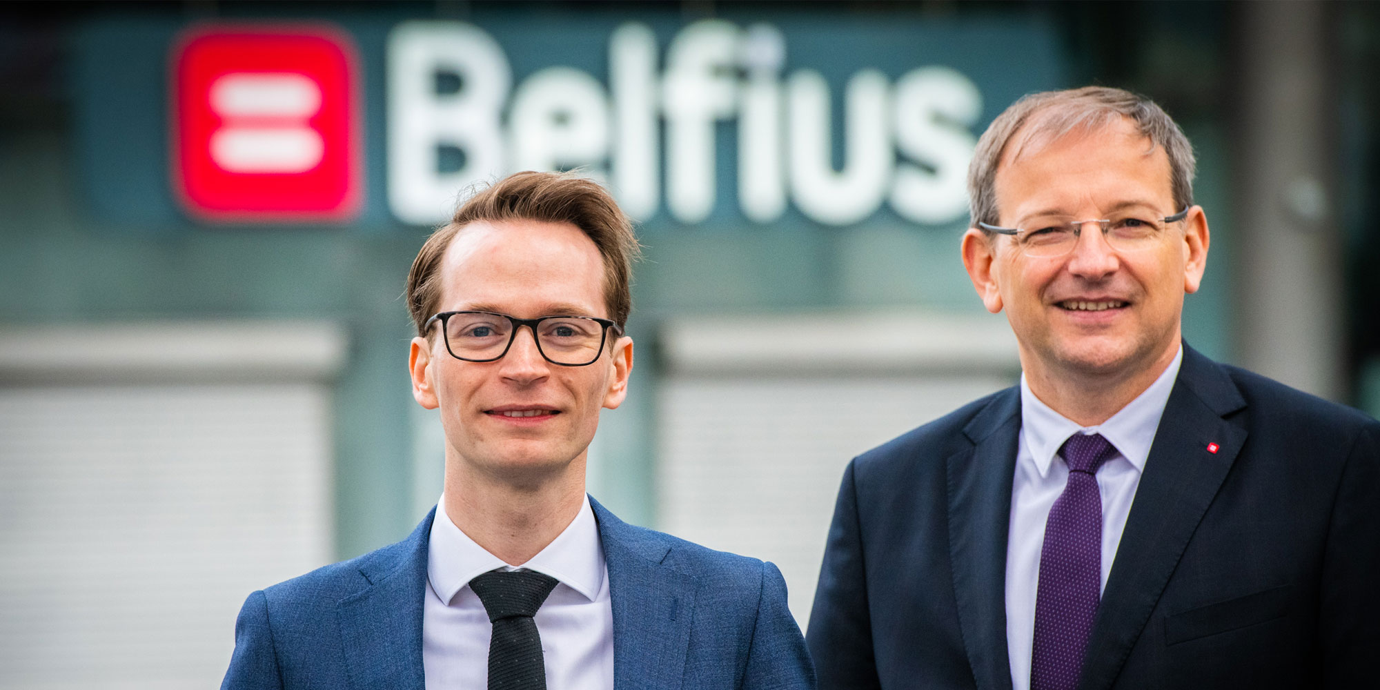 Two people wearing a suit and tie smiling at the camera