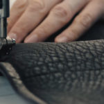 A close up of a hand sewing leather