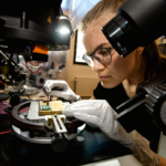 Female scientist wearing plastic gloves while examining a microchip in quantum technology lab.