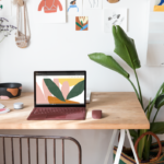 een bureau met laptop en een vaas van bloemen op een lijst