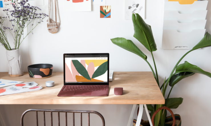 een bureau met laptop en een vaas van bloemen op een lijst