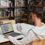en mand ved hjælp af en bærbar computer sidder på toppen af en bog hylde