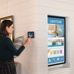 Een vrouw in een meubelwinkel houdt een kussen vast en gebruikt een tablet die aan de muur van de winkel bevestigd is