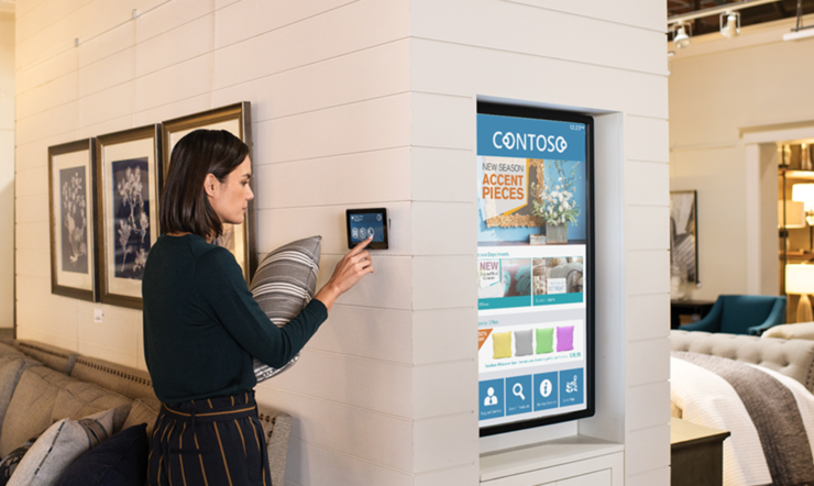 Een vrouw in een meubelwinkel houdt een kussen vast en gebruikt een tablet dat aan de winkelmuur hangt