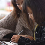 a woman and child sitting at a table using a laptop