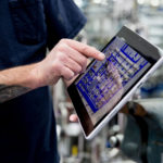 Man with a tattoo pointing at a tablet in a factory