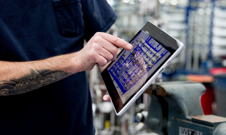 Man with a tattoo pointing at a tablet in a factory