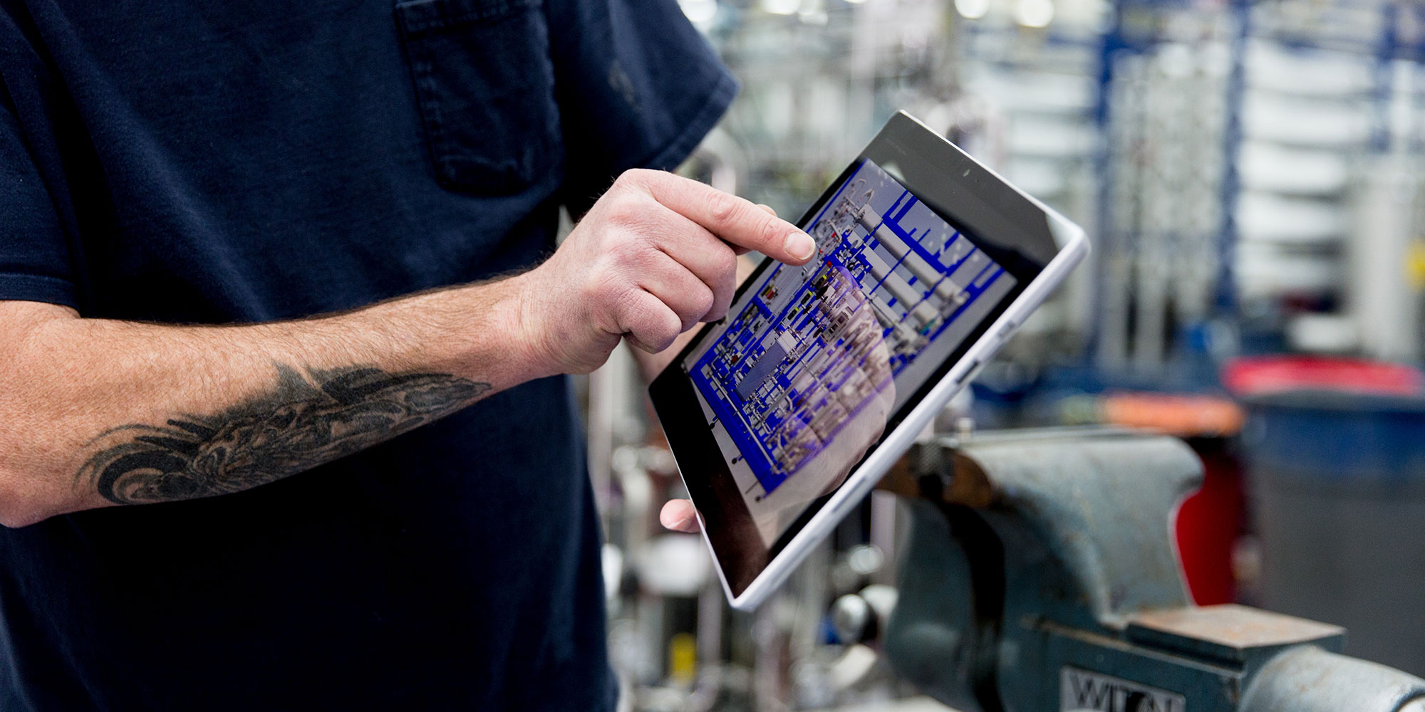 Man with a tattoo pointing at a tablet in a factory