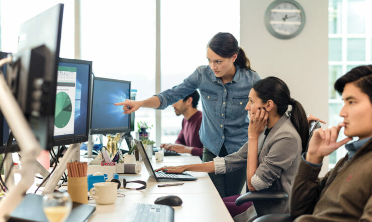 um grupo de pessoas sentadas numa secretária à frente de um computador a analisar dados.