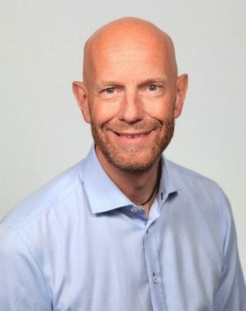 en mann iført briller og smiler på kameraet