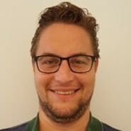 en mann iført briller og smiler på kameraet