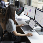 woman in front of two screens and a laptop