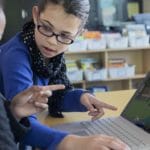 2 young girls playing Minecraft in front of a laptop