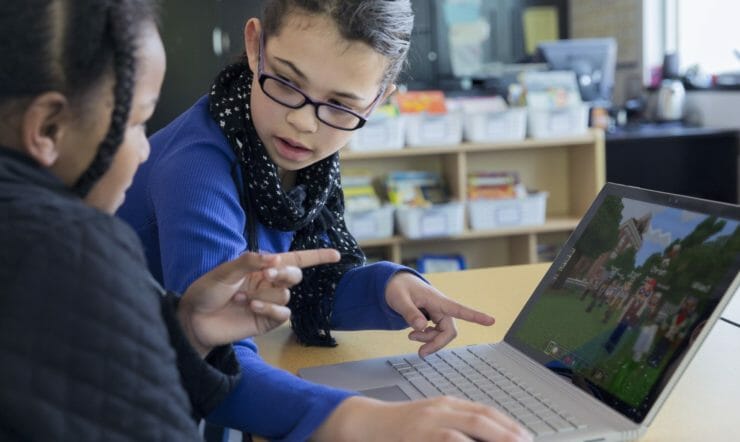 2 young girls playing Minecraft in front of a laptop