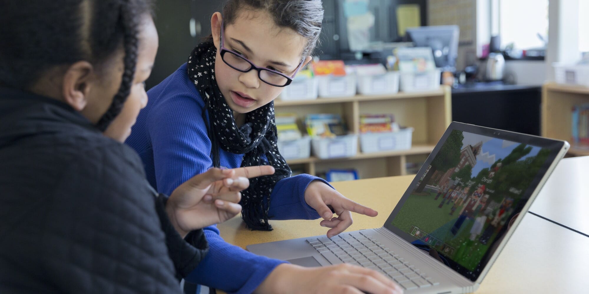Kaksi nuorta tyttöä pelaa Minecraftia kannettavalla tietokoneella