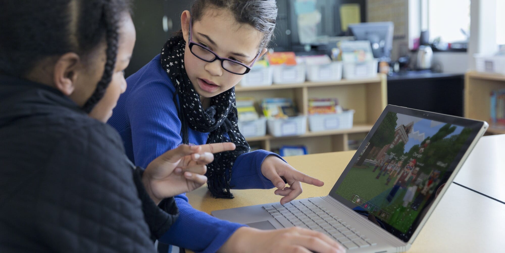 2 young girls playing Minecraft in front of a laptop