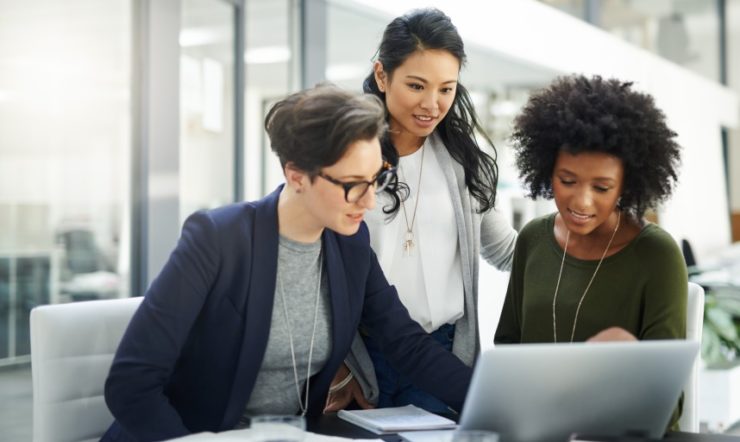 Three women working on a laptop together.