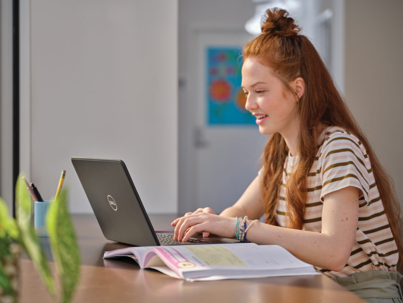 Student werkt aan haar laptop terwijl ze aan een bureau zit. Scherm is niet zichtbaar.