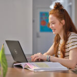 Student werkt aan haar laptop terwijl ze aan een bureau zit. Scherm is niet zichtbaar.