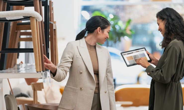 Two women in a furniture shop looking at color tones on a tablet