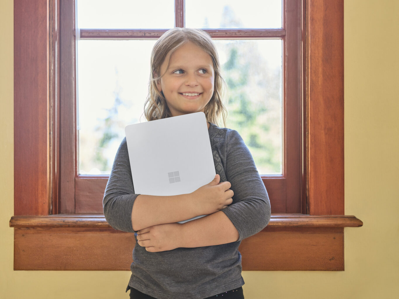 Volksschülerin steht mit einem Surface SE Laptop in einer Schulklasse.