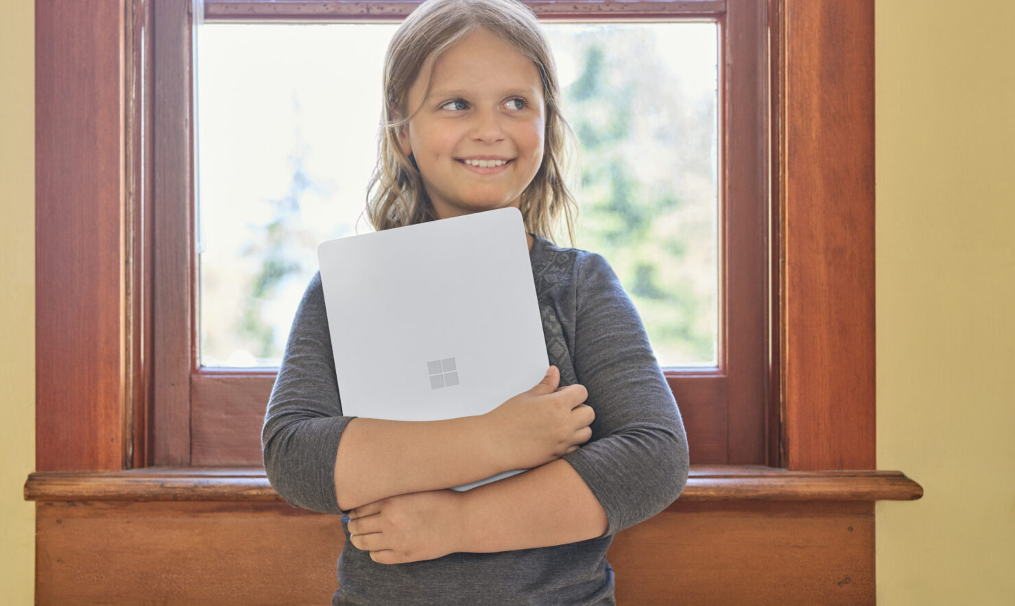 Volksschülerin steht mit einem Surface SE Laptop in einer Schulklasse.