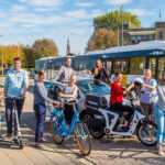 People riding bikes, scooters and a car with a bus in the background