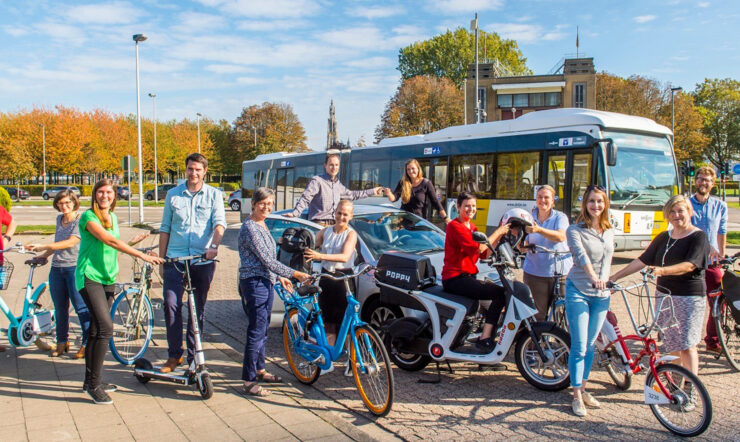 People riding bikes, scooters and a car with a bus in the background