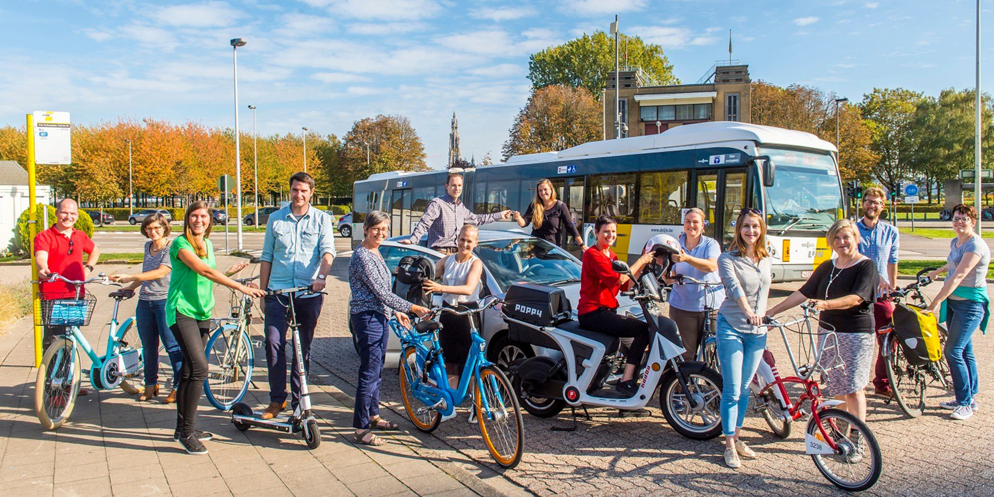 People riding bikes, scooters and a car with a bus in the background