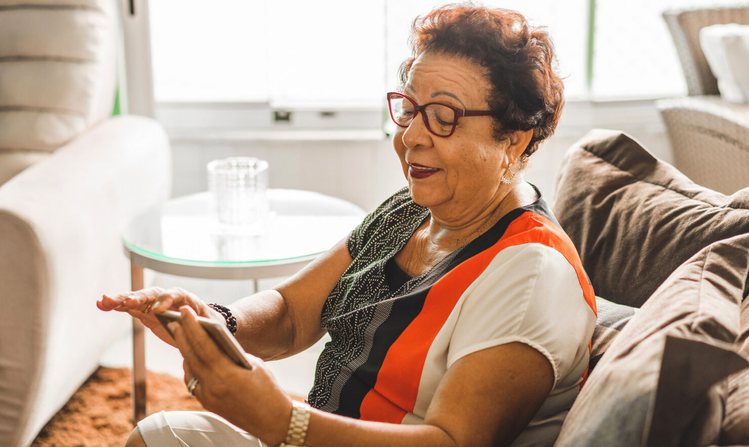 Senior woman sitting in a couch while using a smartphone