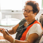 Senior woman sitting in a couch while using a smartphone