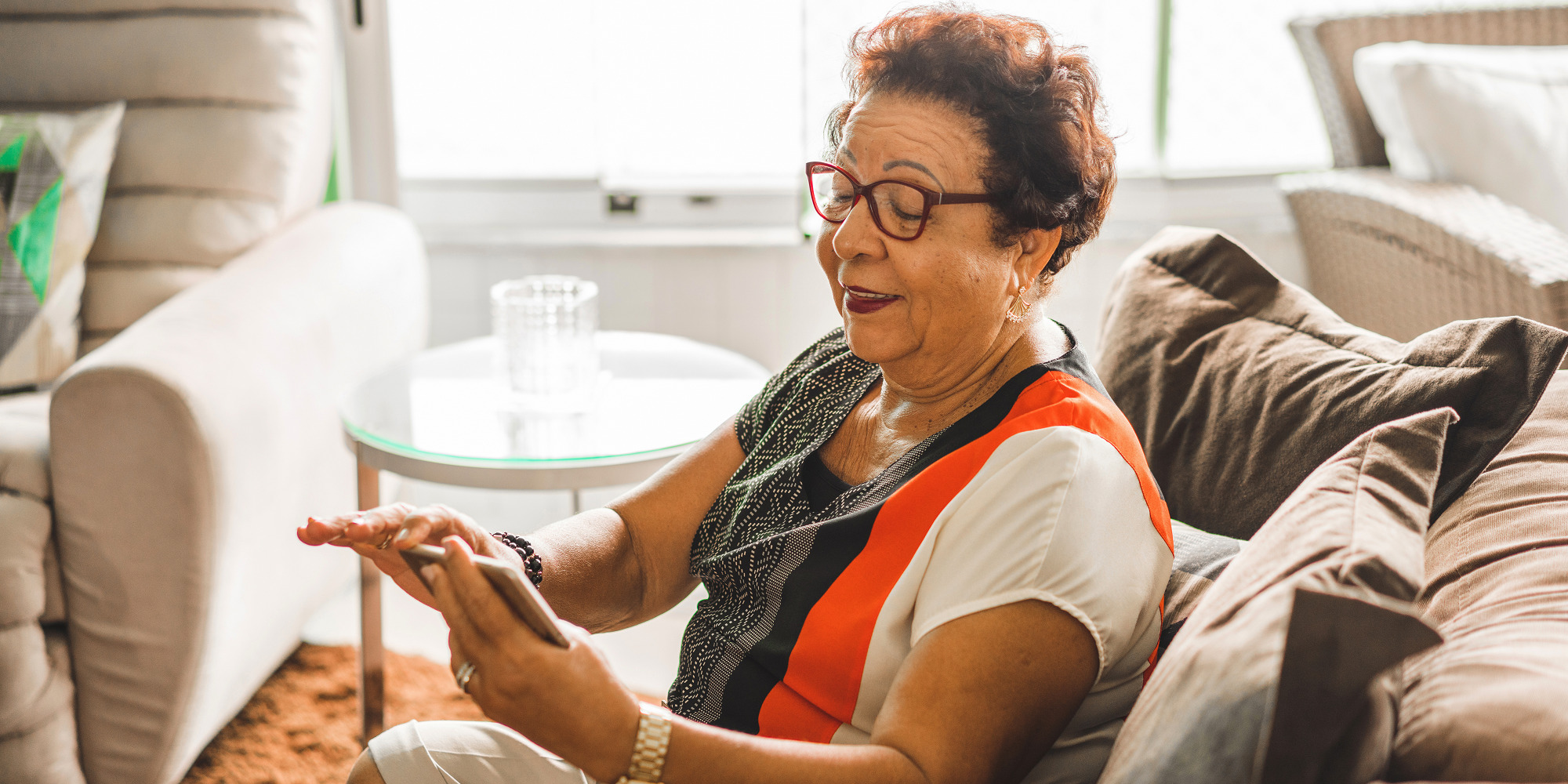 Senior woman sitting in a couch while using a smartphone