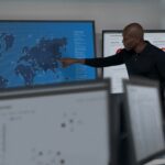 CISO (chief information security officer) collaborating in a security operations center. Keywords: Security; operations; man; wall map; soc; war room; Microsoft Defender for Cloud; threat hunting